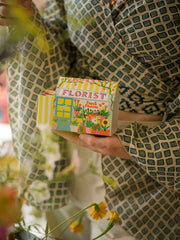 A hand holding the Florist house matchbox beside flowers
