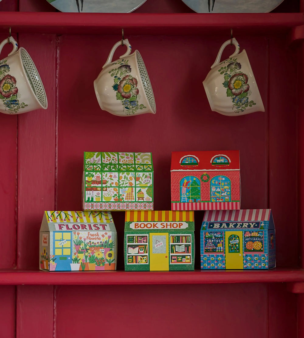 Several house matchboxes lined up on a red shelf